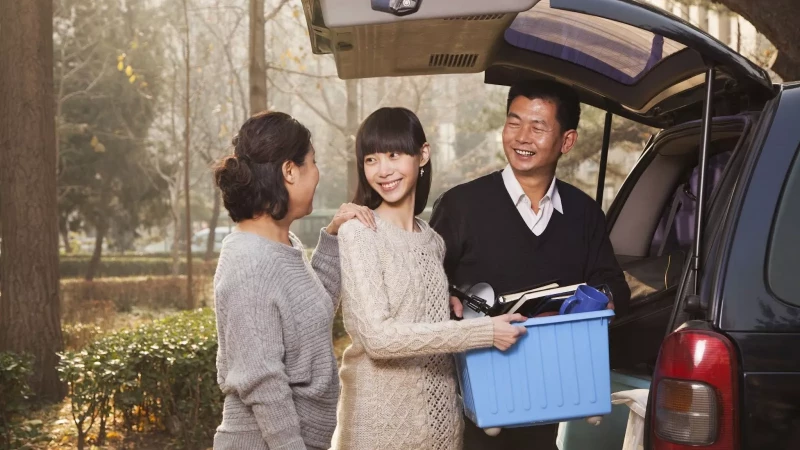 parents with young adult child helping carry college belongings