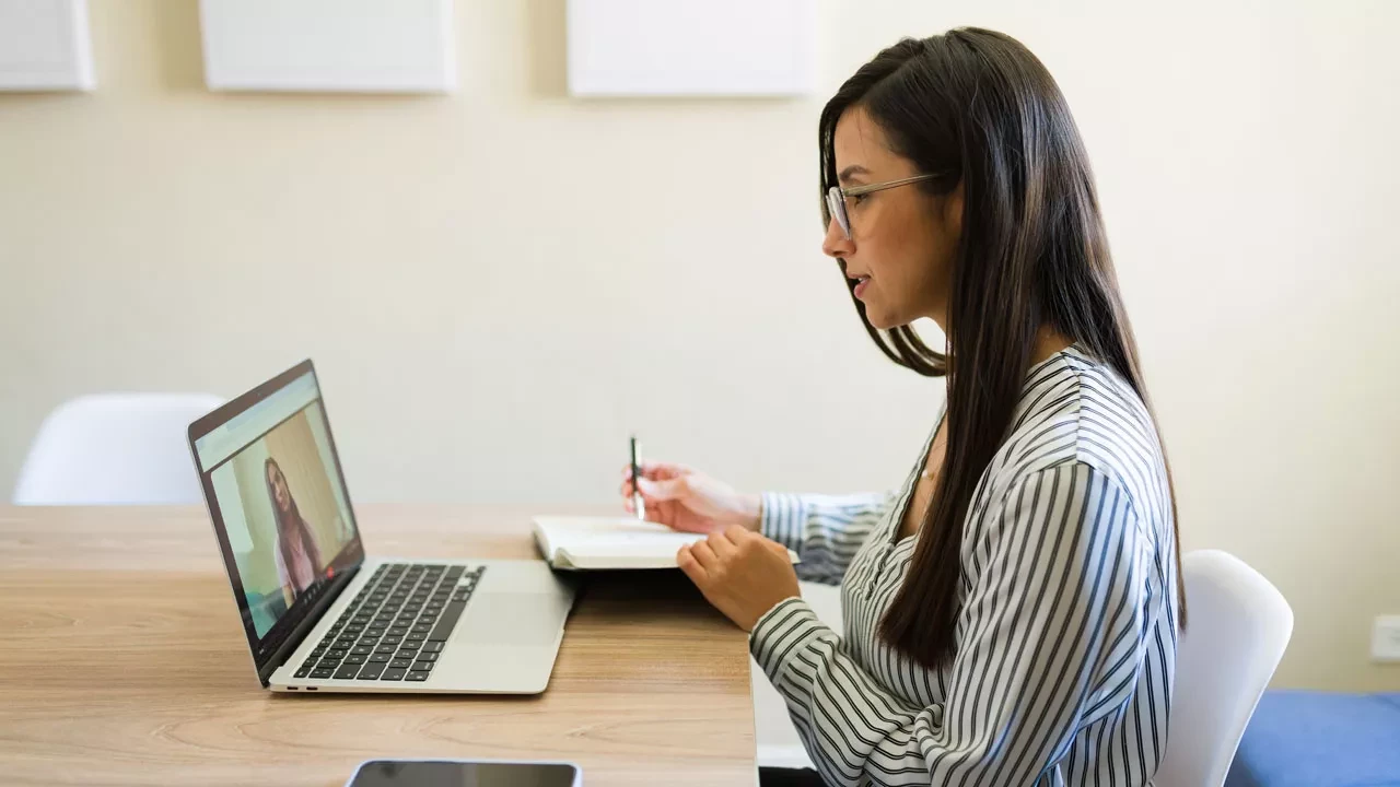 Woman sitting at a desk taking notes with a laptop