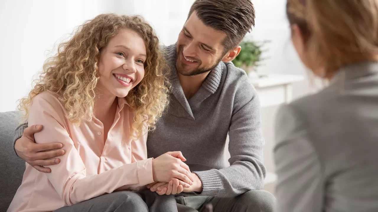 a couple smiling together on a couch talking to a therapist
