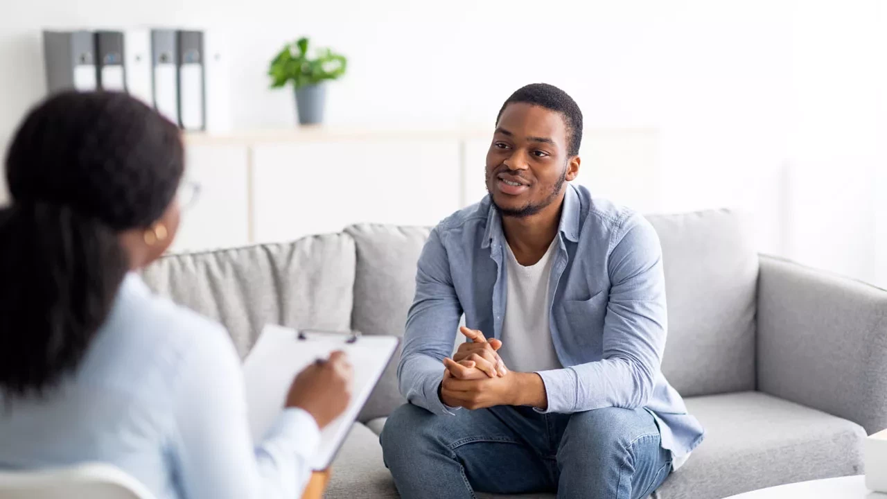 a male sitting on a couch talking to someone taking notes