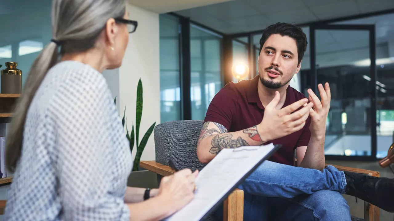 Young man talking to a therapist holding a clipboard