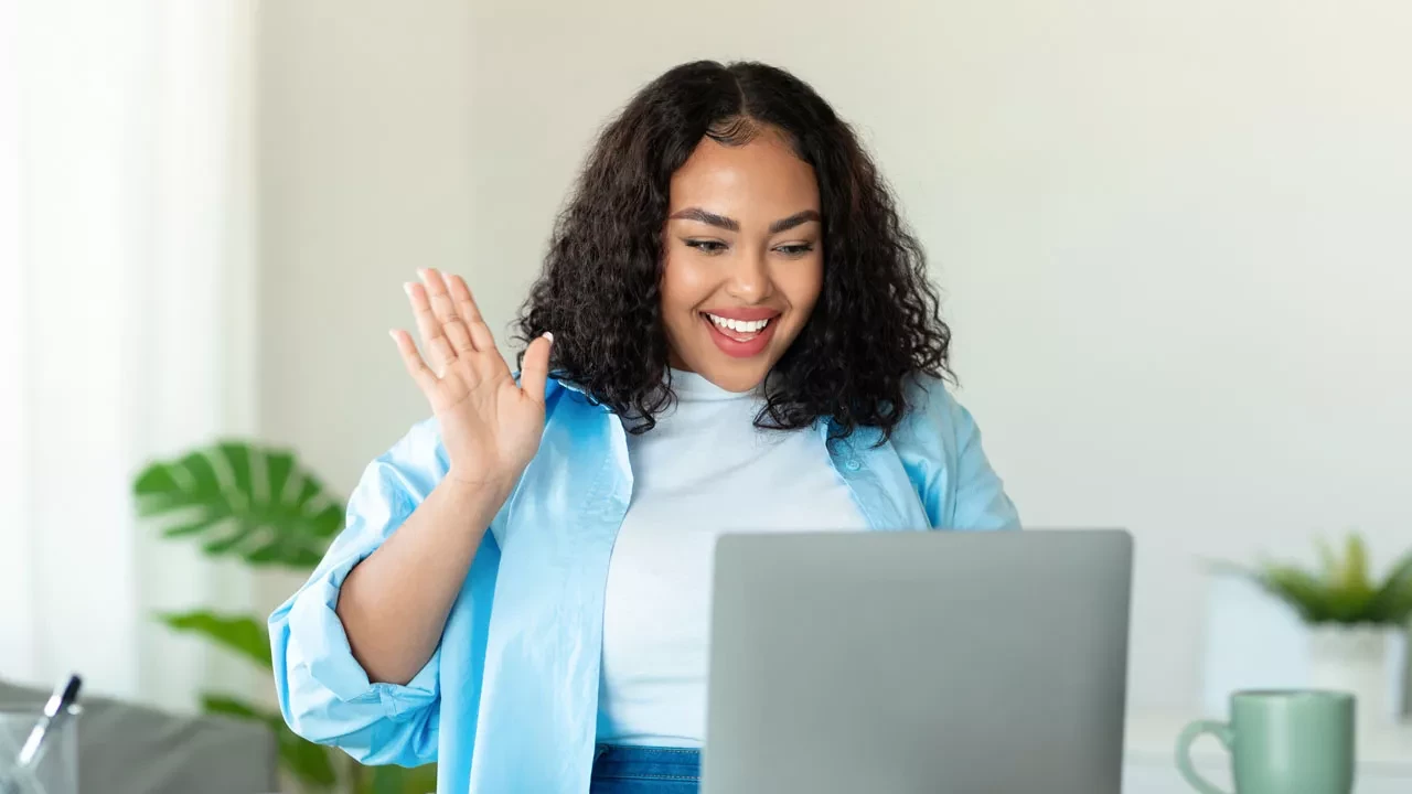 Woman smiling and waving at her laptop camera