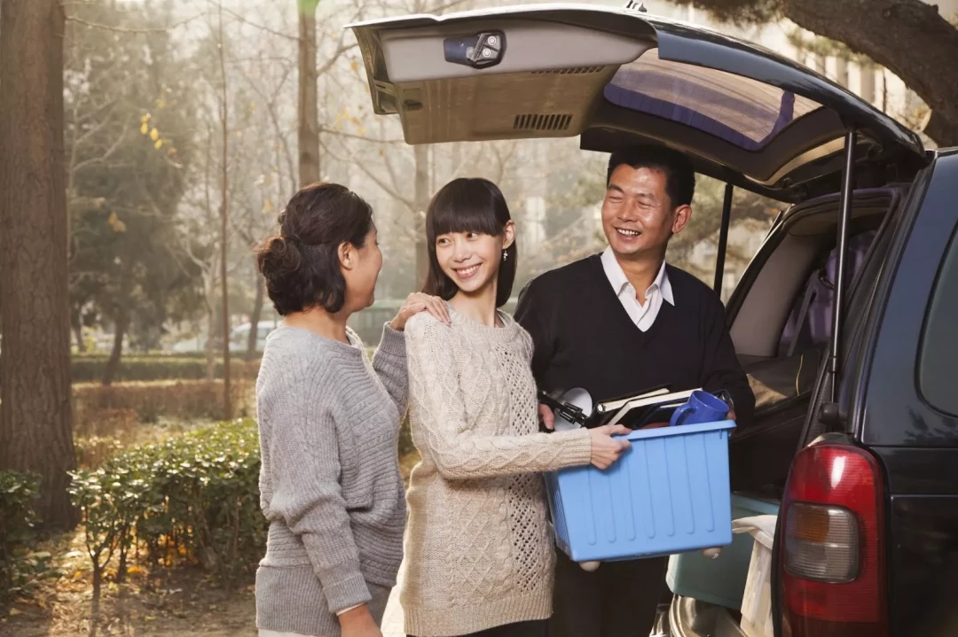 parents with young adult child helping carry college belongings